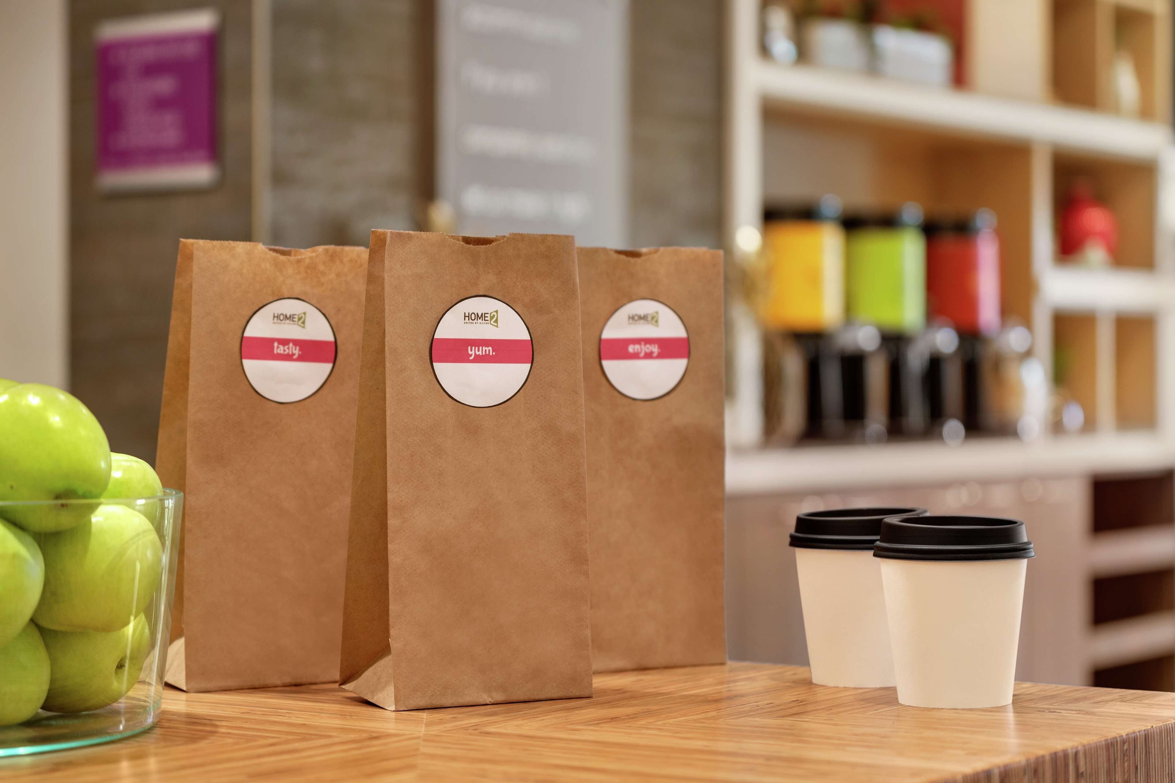 Three brown paper bags with labels and two white disposable cups with black lids on a wooden surface.