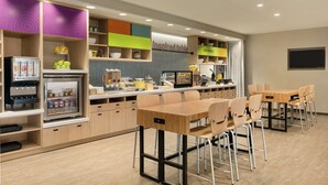 A modern kitchen area with a refrigerator, shelves with food items, and a dining table with chairs. - Home2 Suites by Hilton Ephrata (Ephrata)