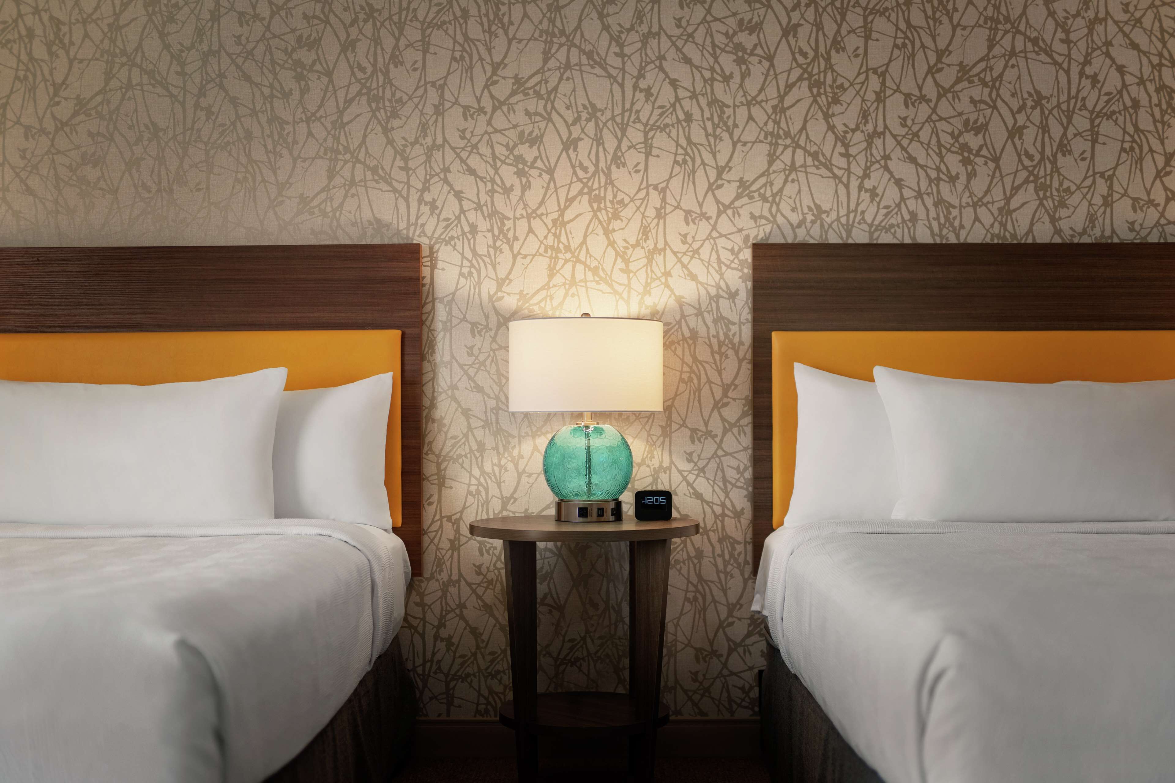 A hotel room with two beds, a nightstand with a lamp, and a clock.