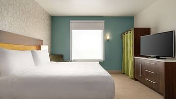 A hotel room with a bed, a television, a window with curtains, and a wall with a patterned design.