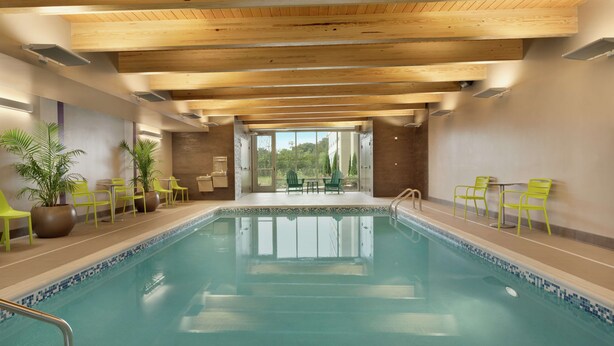 A swimming pool with a view of the outdoors, surrounded by chairs and potted plants. - Home2 Suites by Hilton Ephrata (Ephrata)