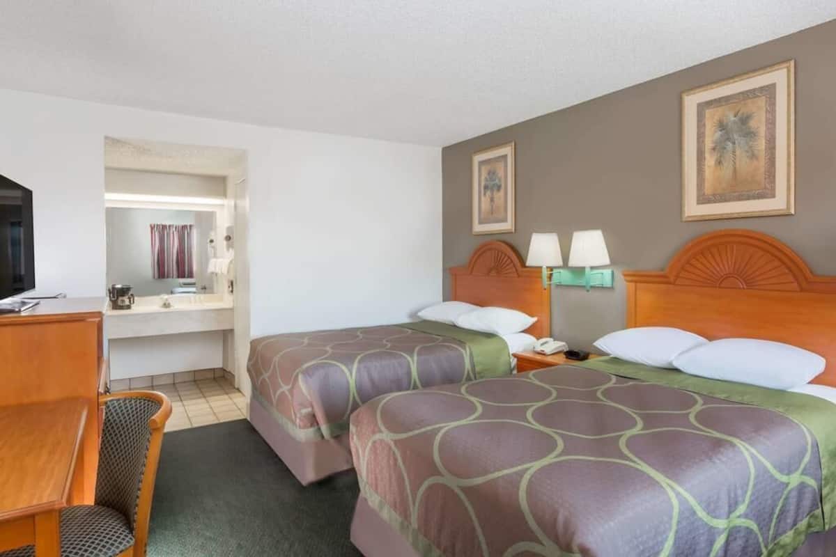 A hotel room with two beds, a desk, a chair, a TV, and a bathroom visible through an open door.