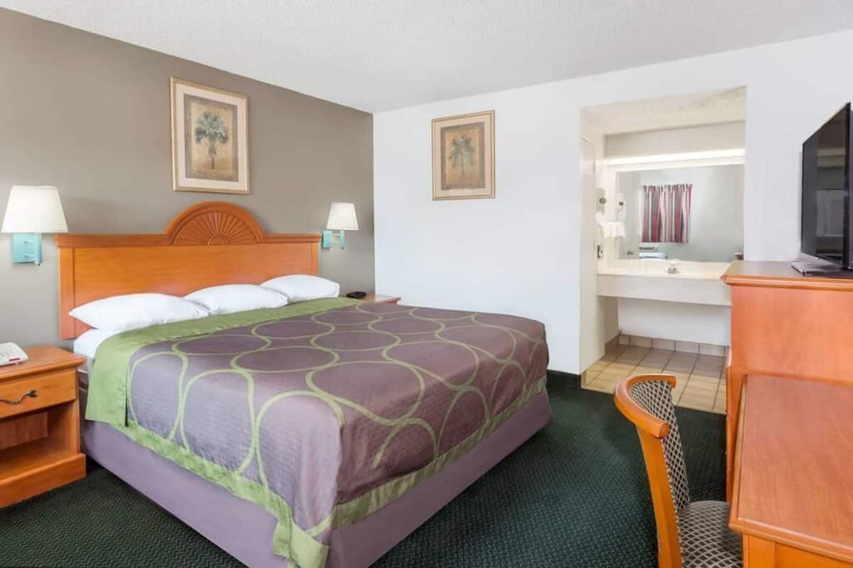 A hotel room with a bed, nightstands, a desk, a chair, a television, and a bathroom visible through an open door.