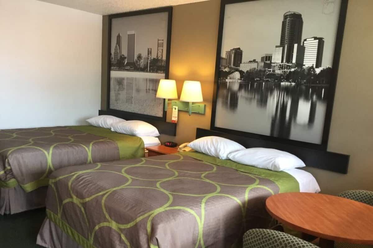 A hotel room with two beds, a table, and two wall-mounted lamps.