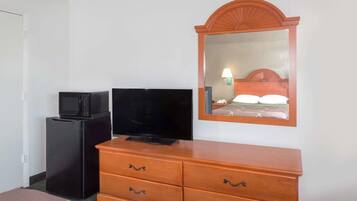 A hotel room with a wooden dresser, a television on a black stand, and a mirror with a wooden frame.