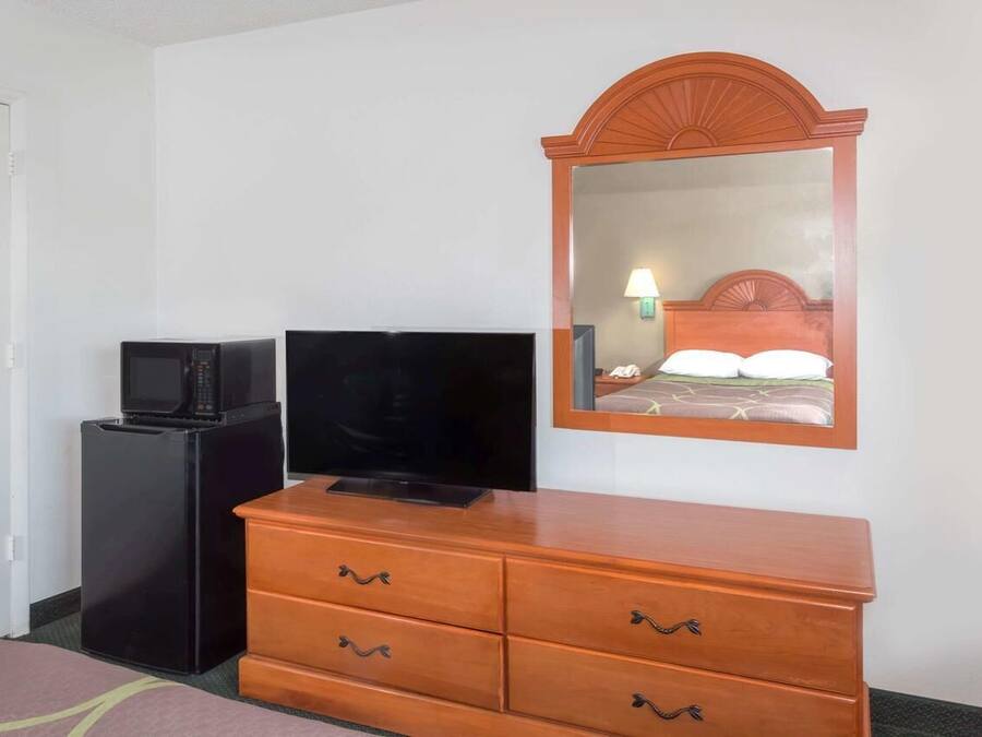 A hotel room with a wooden dresser, a television on a black stand, and a mirror with a wooden frame.