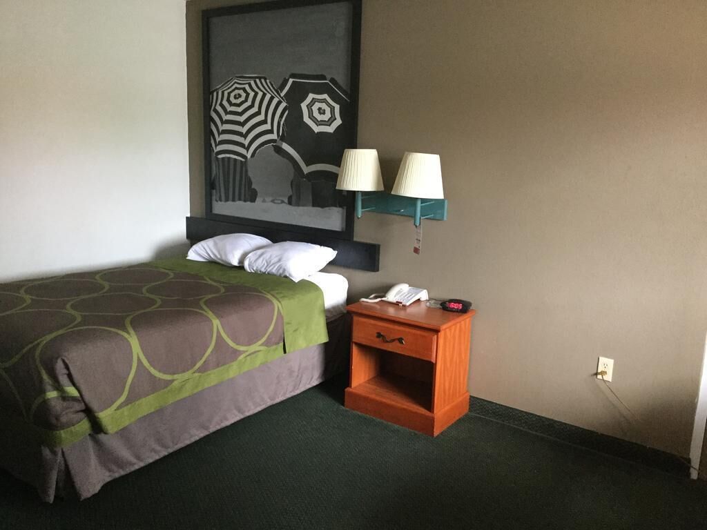 Quarto de hotel com cama, mesa de cabeceira com abajur, telefone e uma obra de arte na parede.