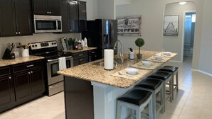 A modern kitchen with dark cabinets, stainless steel appliances, granite countertops, and a central island with bar stools.