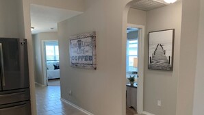 A hallway with a refrigerator, a 'Live Laugh Love Coffee' sign, and a framed picture on the wall.