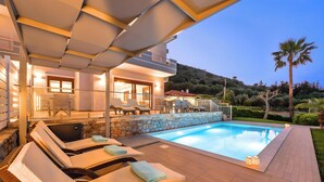 A poolside area with lounge chairs and a stone wall. - Sunlight Villa Heated Pool Sea View (Georgioupoli)