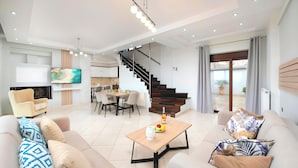 A modern living room with a sofa, coffee table, and a TV. There is a staircase leading to a balcony with a view. - Sunlight Villa Heated Pool Sea View (Georgioupoli)