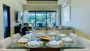 Un coin repas avec une table en verre dressée pour le repas, un canapé et un téléviseur en arrière-plan.