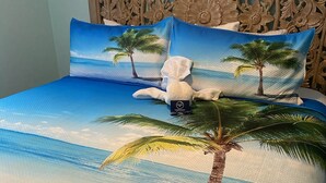 A bed with a beach scene cover, a wooden headboard, and a white pillow.