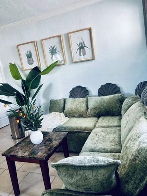 A living room with a sectional sofa, a coffee table, a potted plant, and framed botanical prints on the wall. - The Monterey offers this view in 45 sec (Redington Shores)