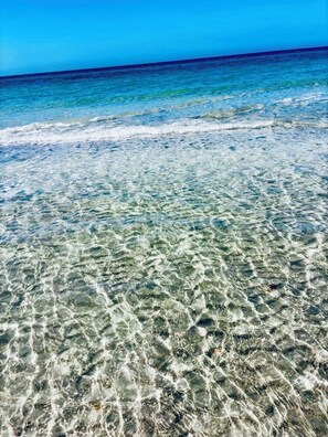 A clear beach with visible underwater patterns and a calm sea.