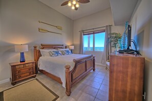 A bedroom with a wooden bed, a nightstand, a dresser, a ceiling fan, and a window with a view.