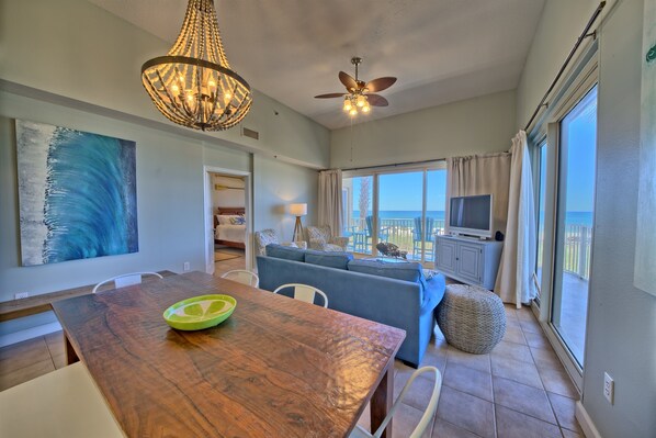 A spacious living area with a dining table, blue sofa, and a large window offering a view of the ocean.