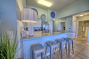 Une cuisine dotée d’un comptoir en granit, de tabourets de bar, d’une grande lampe et d’assiettes décoratives accrochées au mur.
