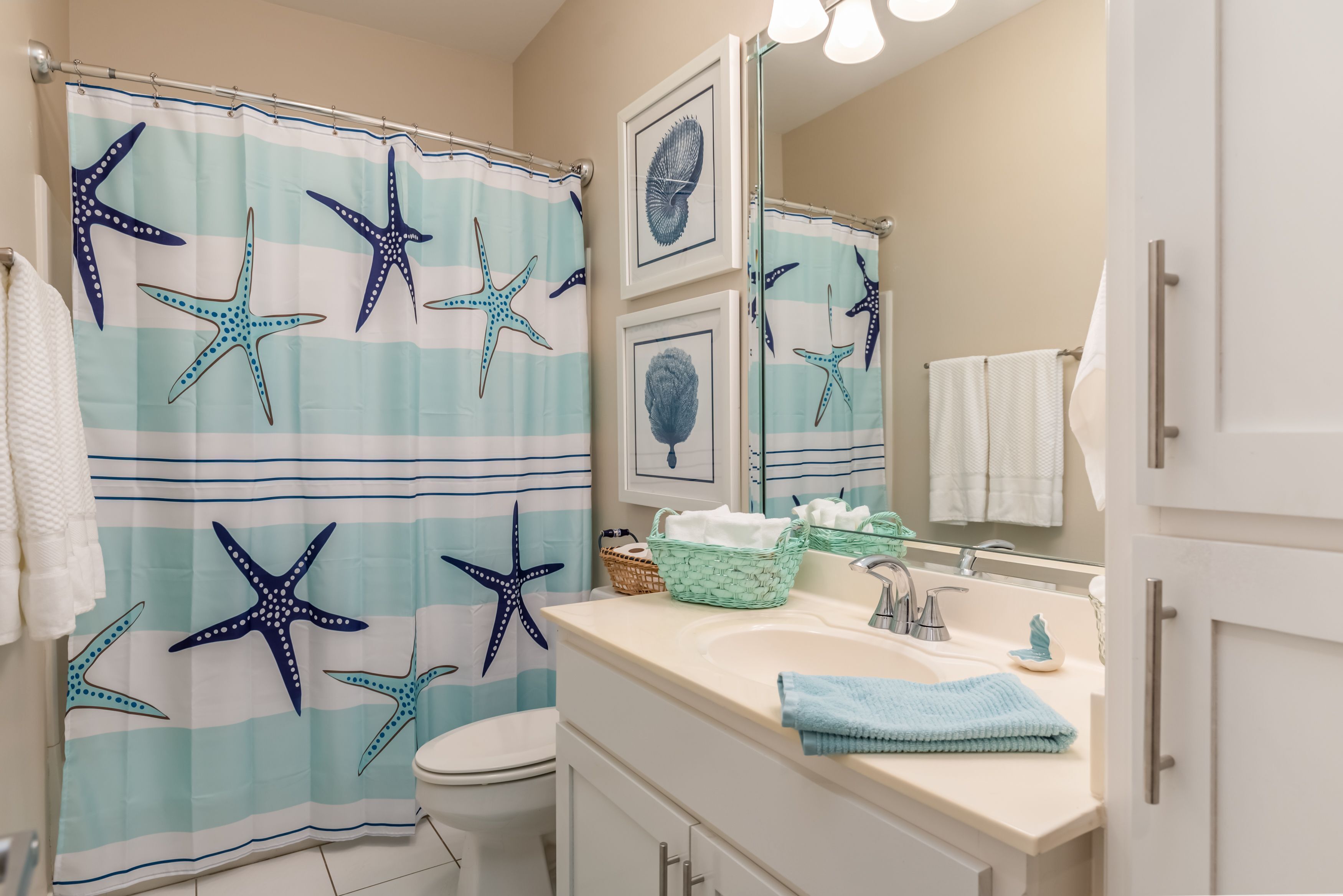 A bathroom with a starfish shower curtain, a sink with a mirror, and a toilet.
