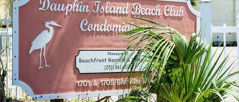 A sign for Dauphin Island Beach Club Condominium with a contact number and address.