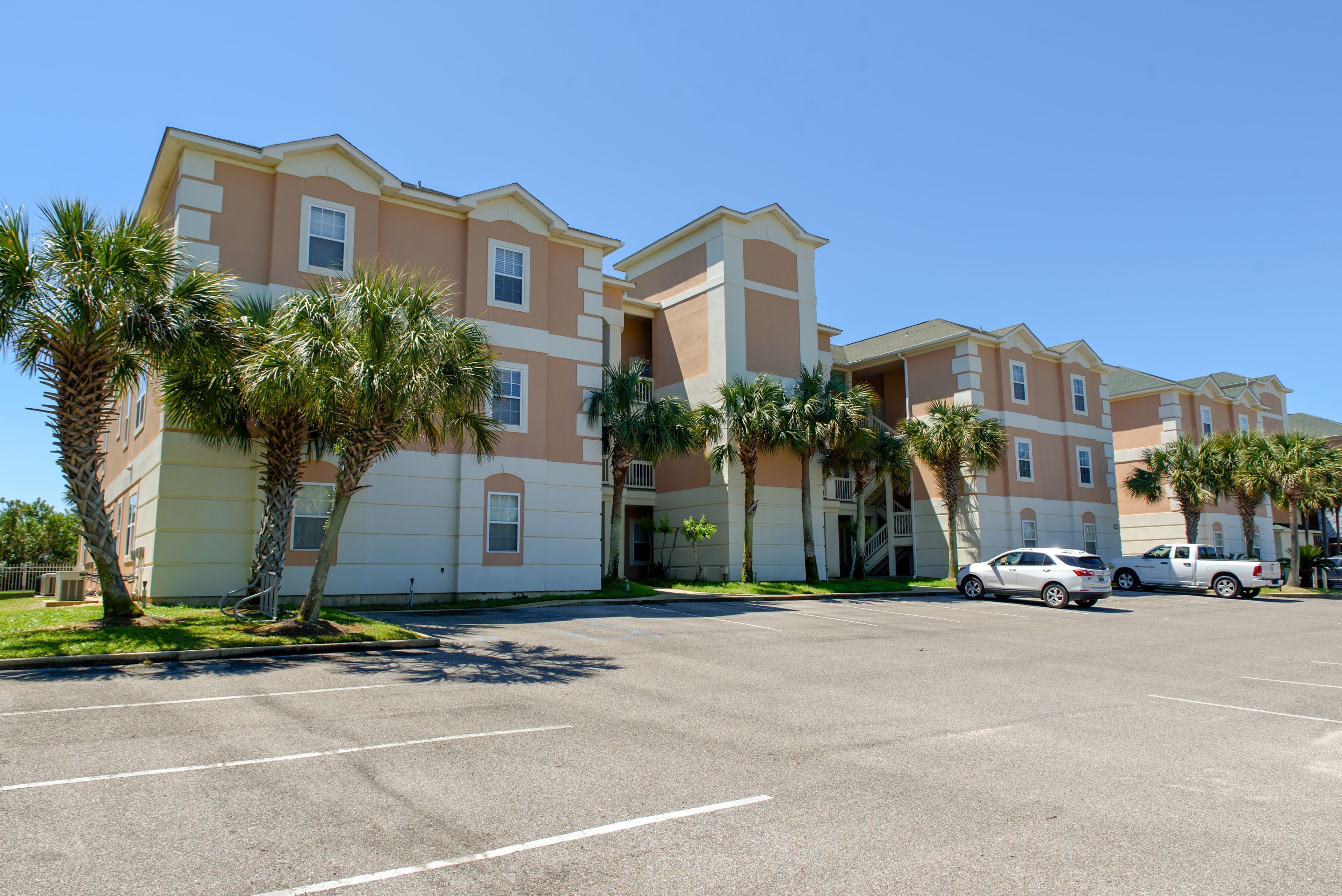 A multi-story hotel with a parking lot and palm trees in front.