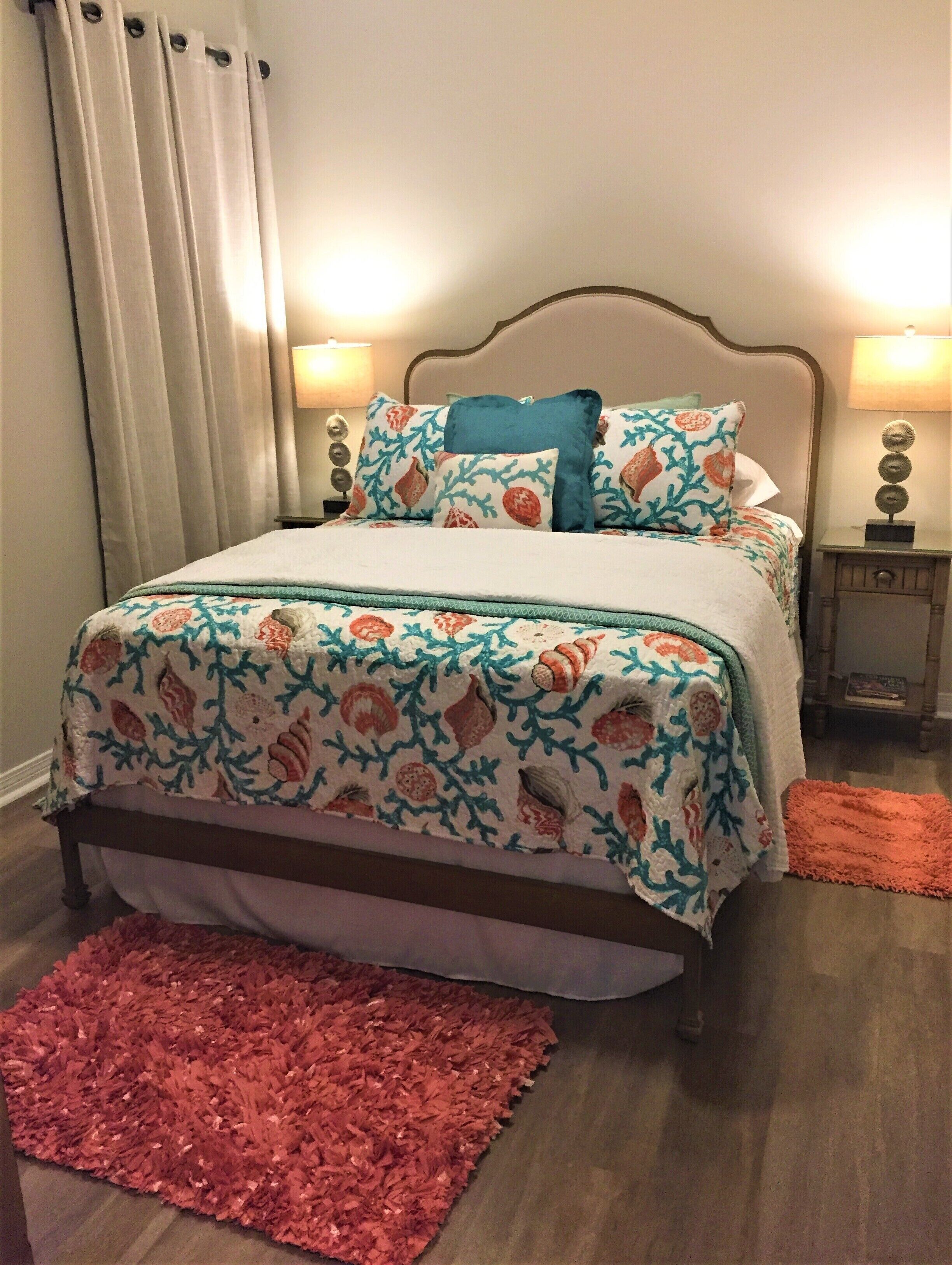 A bed with floral bedding, two bedside lamps, and a red rug.