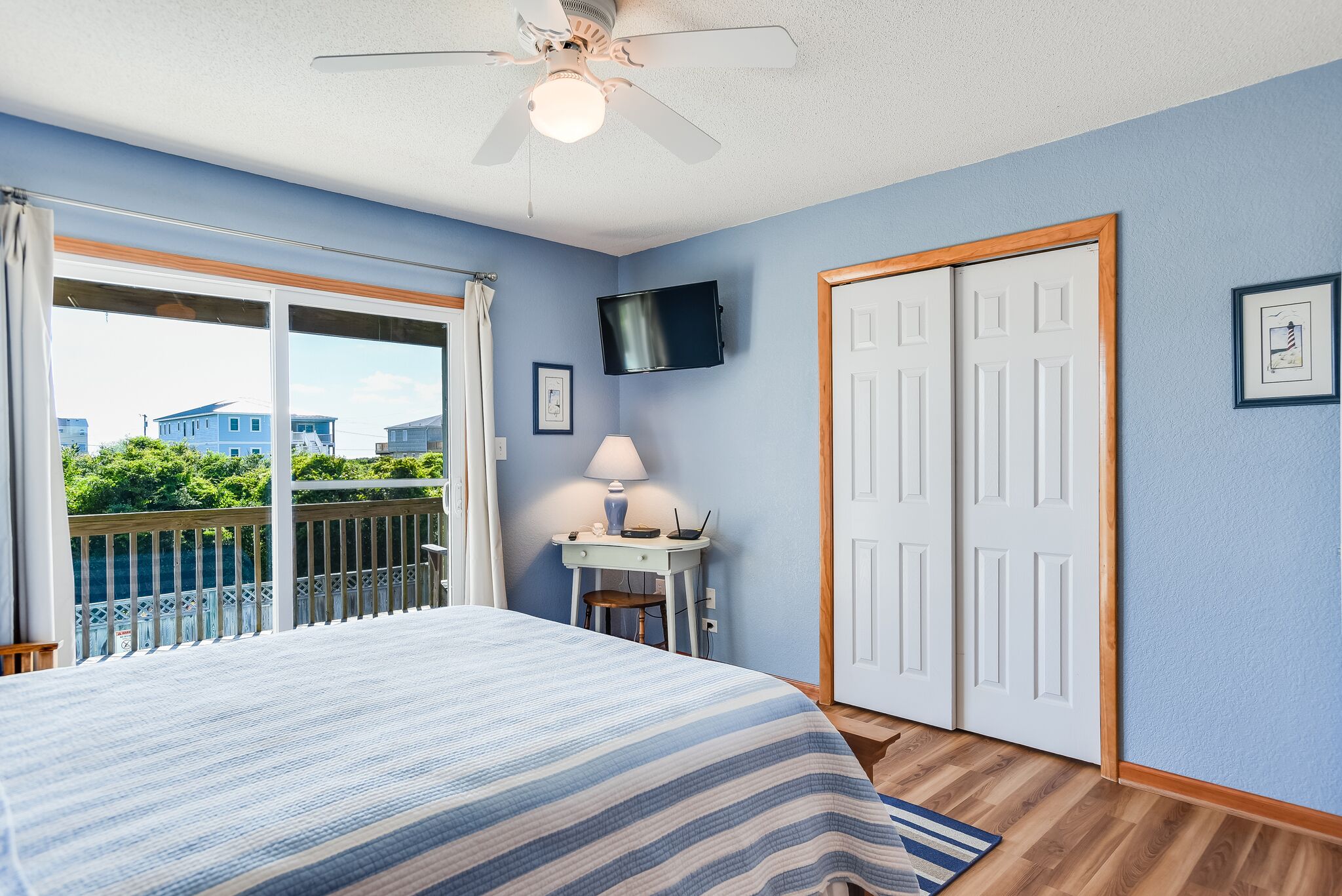 A bedroom with a bed, a desk, a chair, a TV, and a balcony.