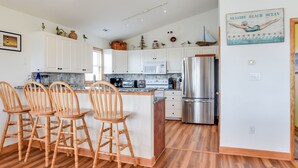 Una cocina con armarios blancos, un refrigerador de acero inoxidable, sillas de madera y un letrero decorativo en la pared.