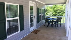 A covered porch with a wooden deck, a table with chairs, and a door with a window.