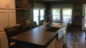 A kitchen with a large island, dark countertops, and wooden cabinetry. There are multiple chairs around the island and a dining table in the background.
