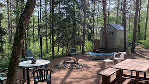 Un campamento arbolado con una cabaña pequeña, mesas de picnic y sillas.