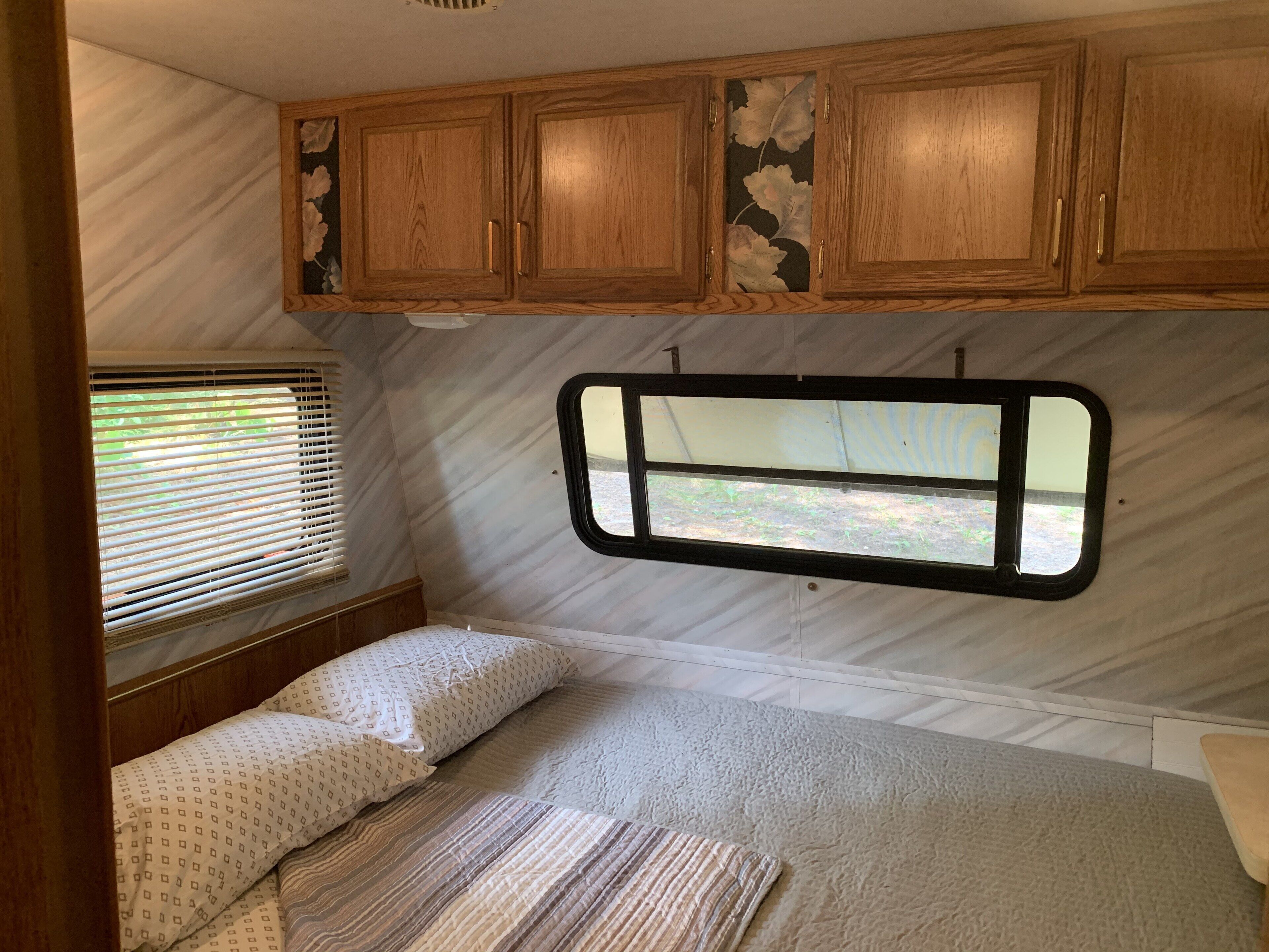 Interior de una caravana compacta con cama, ventana y armarios de madera.
