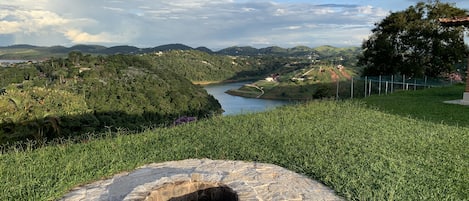 Un foyer en pierre, installé dans un espace herbeux, offre une vue sur un lac et des collines en arrière-plan.
