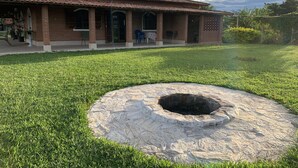 Un edificio de ladrillo con techo de tejas, un césped y un pozo de piedra.