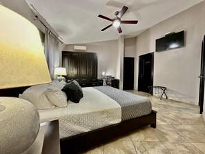 Un dormitorio con cama, ventilador de techo, televisor y armario.