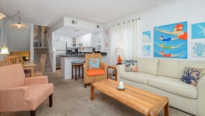 Sala de estar com sofá, cadeiras, mesa de centro e cozinha ao fundo.