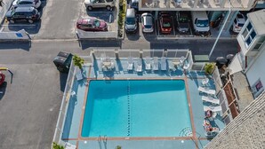 Piscina no terraço com espreguiçadeiras e vista para carros estacionados e edifícios.