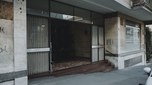 Un bâtiment moderne avec une façade en béton, de grandes fenêtres et un portail métallique à l’entrée.
