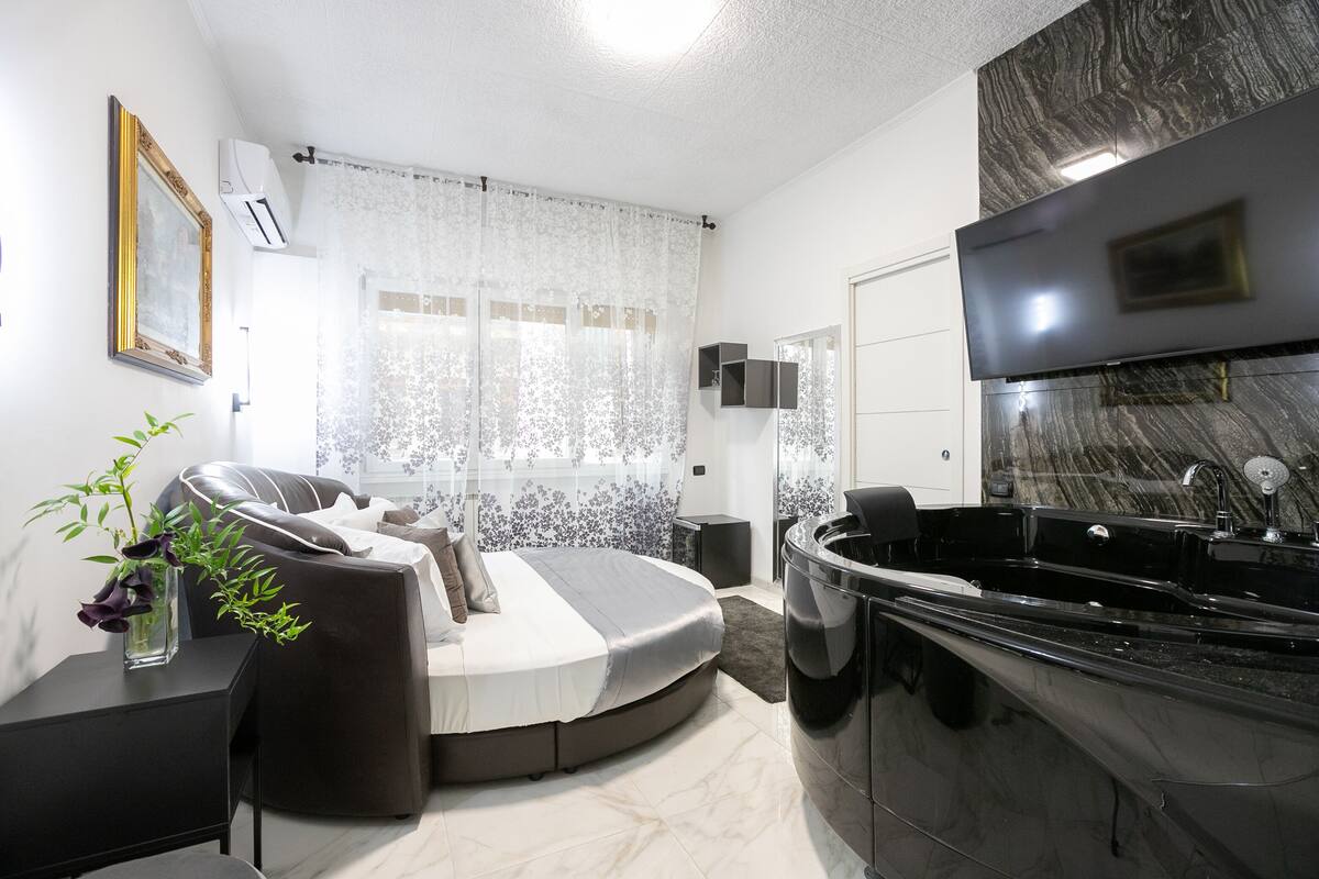 Une chambre à coucher moderne avec un lit aux lignes courbes, une baignoire noire et un sol en marbre.