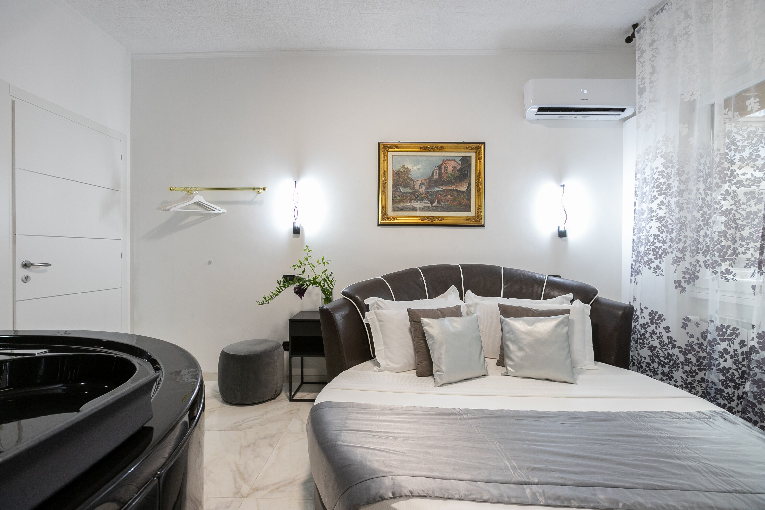 A modern bedroom with a large bed, a side table, a hanging light, a framed picture, and an air conditioning unit.