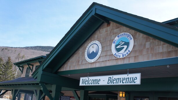A building with a wooden facade, a sign reading "Welcome - Bienvenue," and two circular logos for the Great Glen Trail and Mt. Washington Auto Road. - Wentworth Townhouse - Golf, Hike, Water Falls, Stoy Land!! (Jackson)