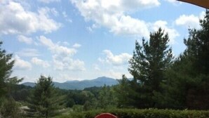 A patio with a round table and two red chairs, a metal lantern, and a view of trees and mountains in the background. - Wentworth Townhouse - Golf, Hike, Water Falls, Stoy Land!! (Jackson)