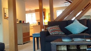 A loft-style living area with a staircase, a sofa, a coffee table, and a kitchen in the background. - Wentworth Townhouse - Golf, Hike, Water Falls, Stoy Land!! (Jackson)