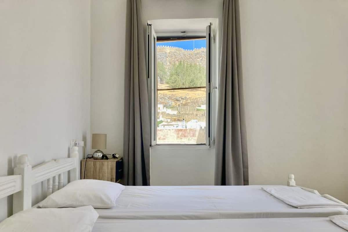 A bedroom with a bed, a nightstand, a lamp, and a window with curtains.