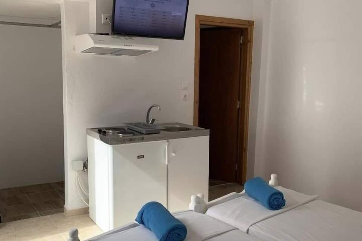 A hotel room with a bed, a small kitchenette, a TV, and a wooden door.