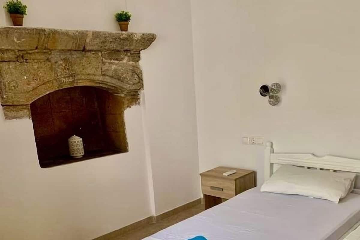 A bedroom with a stone fireplace, a bed with white bedding, a bedside table, and a nightstand.