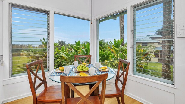 Zona pranzo con un tavolo rotondo, quattro sedie di legno e vista su un giardino tramite ampie finestre.