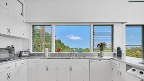 Una cucina moderna con mobili bianchi, un piano di lavoro in acciaio inossidabile, una lavastoviglie e una finestra vista verde.