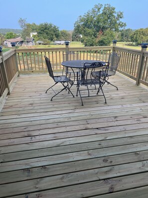 A wooden deck with a metal table and chairs, surrounded by a wooden railing. - Fireside Cabin – a cozy retreat at Truman Lake – relax and unwind! Pet friendly! (Deepwater)