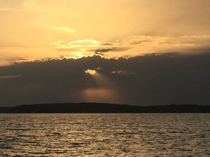 A sunset over a body of water with a silhouette of a landmass in the distance. - Fireside Cabin – a cozy retreat at Truman Lake – relax and unwind! Pet friendly! (Deepwater)